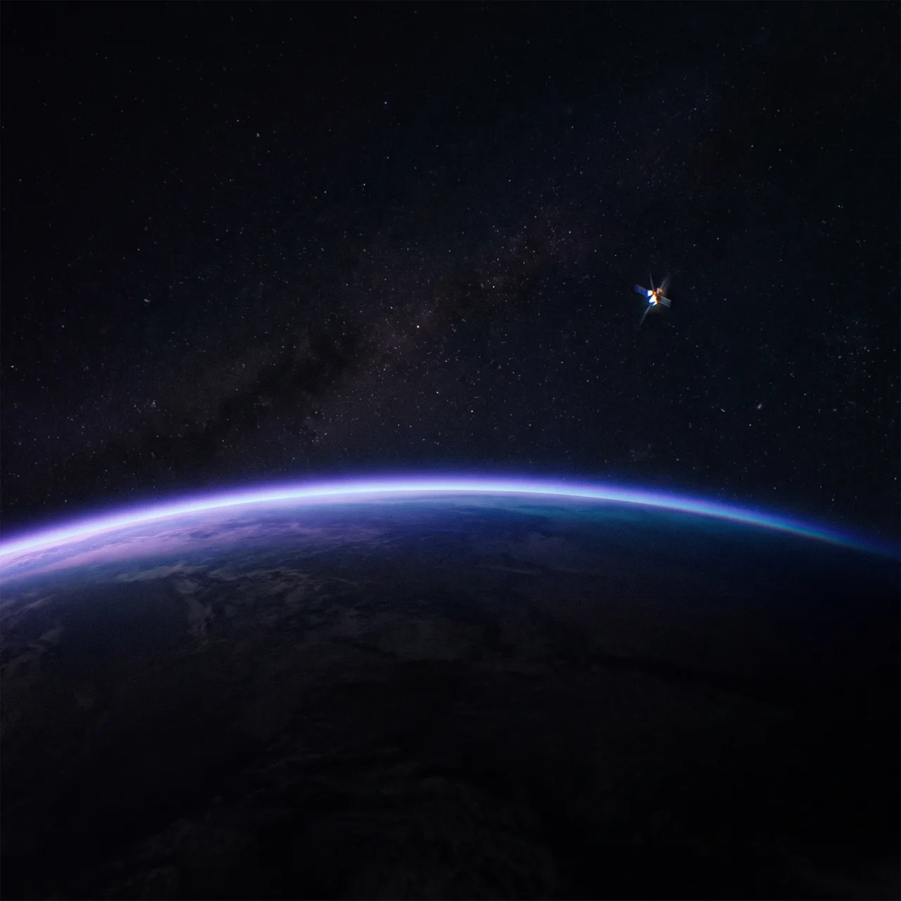 The sunlit limb of a planet seen from orbit — a thin violet arc of atmosphere against deep space, a small satellite catching the light above it
